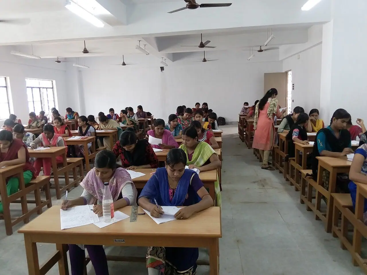Students sit a written class test in a West Bengal government college classroom, March 2016 (Wikimedia Commons photograph by Naba1224, CC BY-SA 4.0)—generic high-stakes pen-and-paper examination setting relevant to NEET integrity probes; not the NTA logo, a seized question paper, or any named 2026 examination hall named in the investigation.